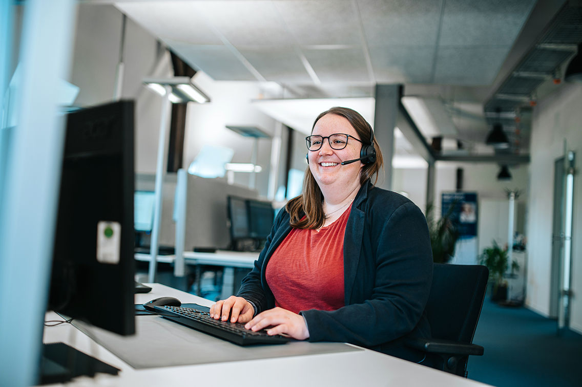 Frau mit Headset sitzt am Computer und bearbeitet ein telefonisches Kundenanliegen