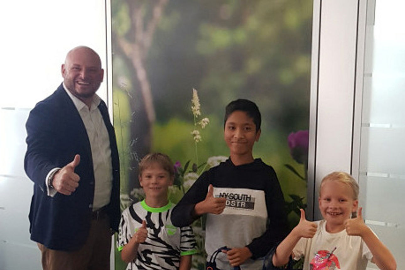 Vorstand steht neben drei Kindern mit Daumen nach oben in unserer Bank