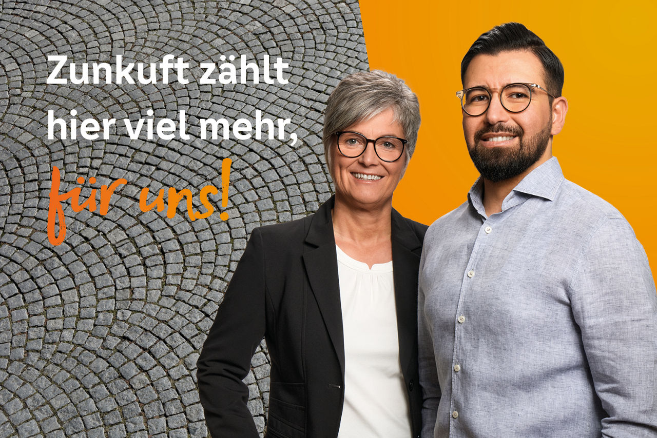 Zwei Kollegen stehen vor orangener Wand