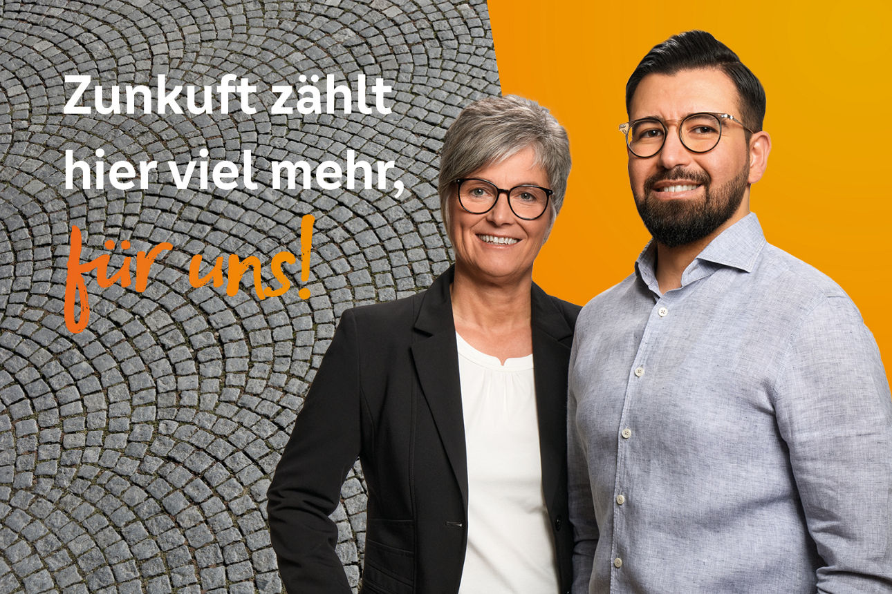 Zwei Kollegen stehen vor orangener Wand