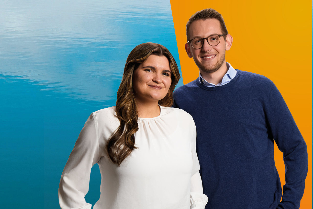 Zwei junge Azubis stehen vor orangem/blauem Hintergrund