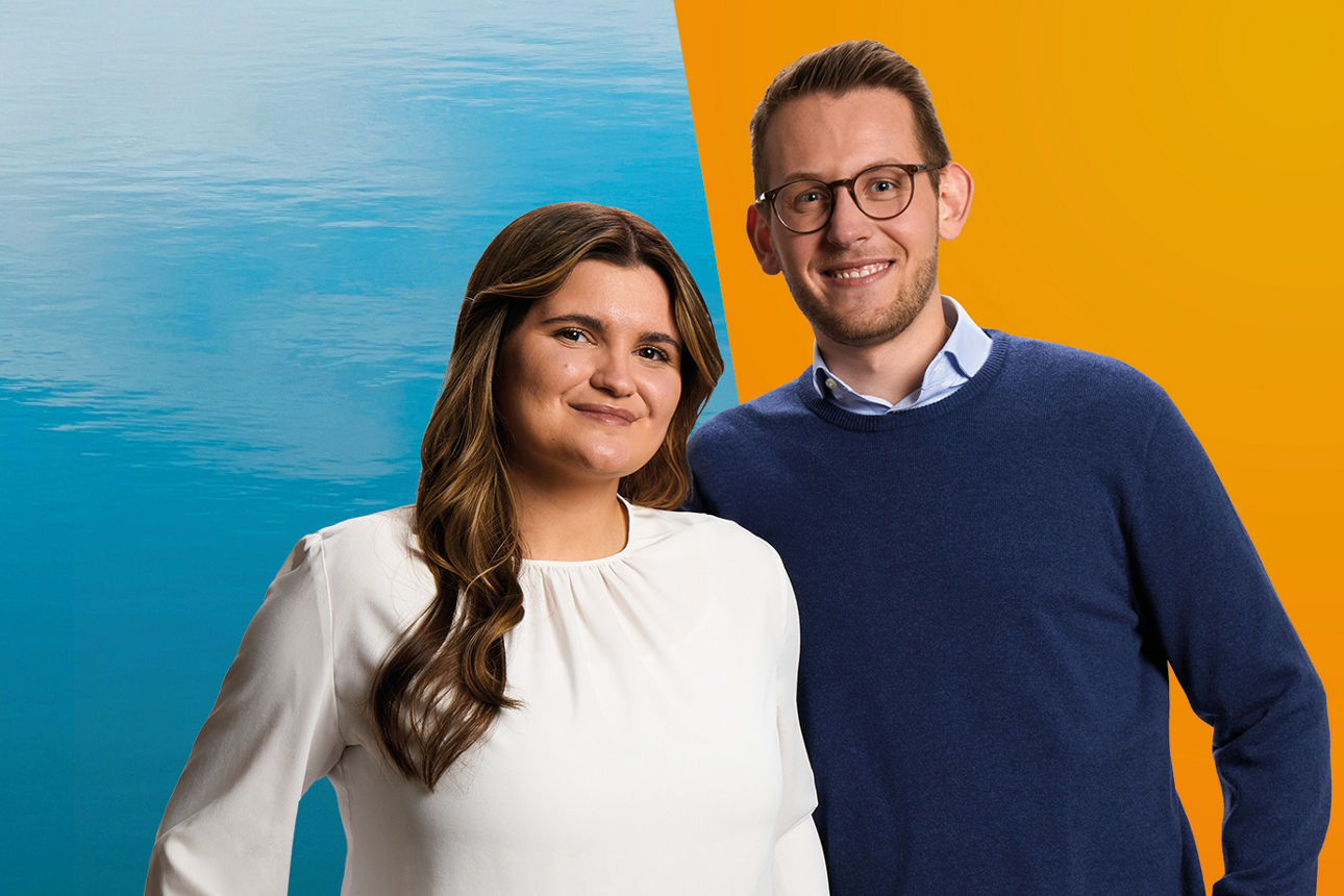 Zwei junge Azubis stehen vor orangem/blauem Hintergrund