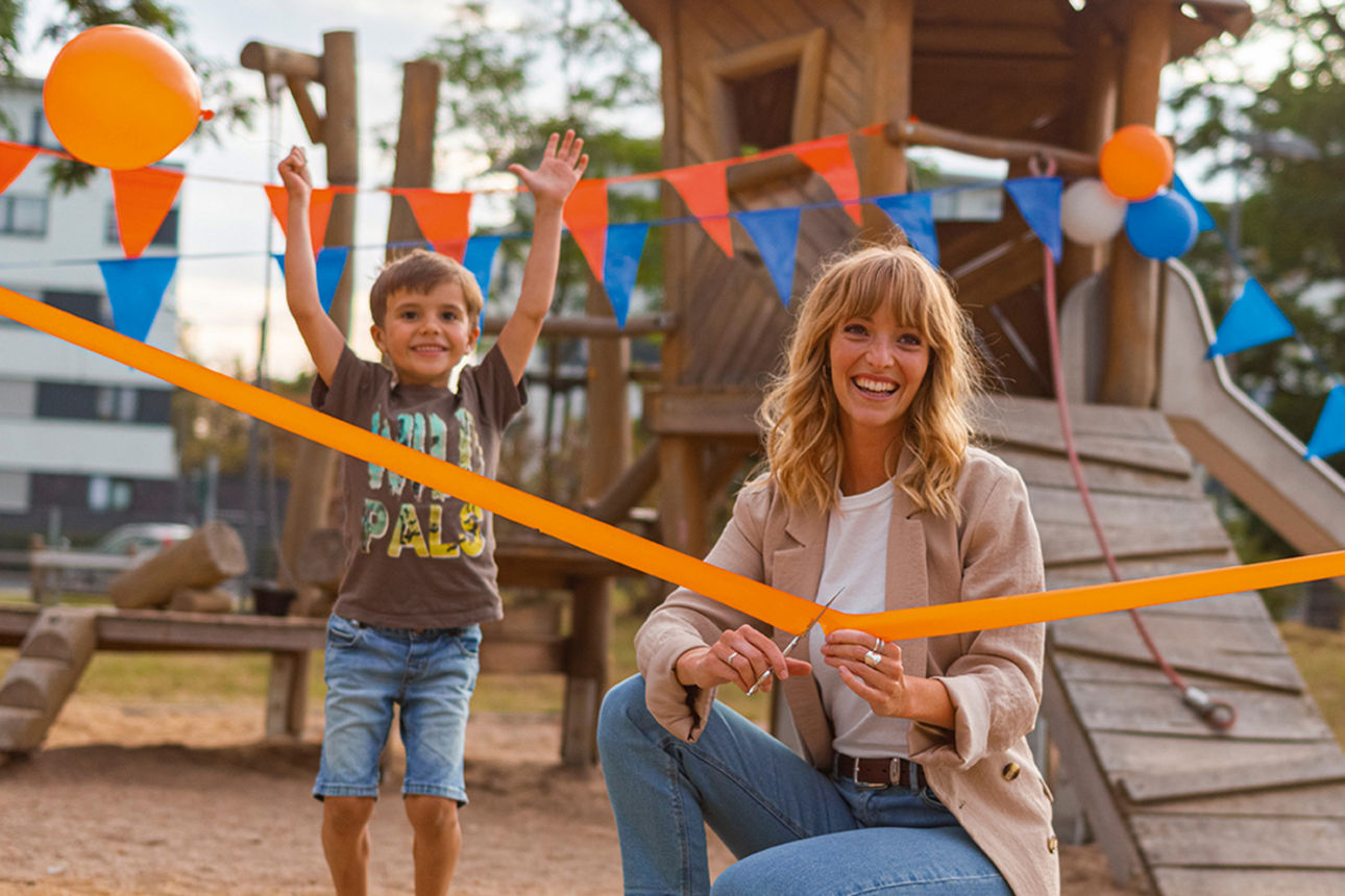 Junge Frau schneidet oranges Band durch bei Spielplatzeröffnung