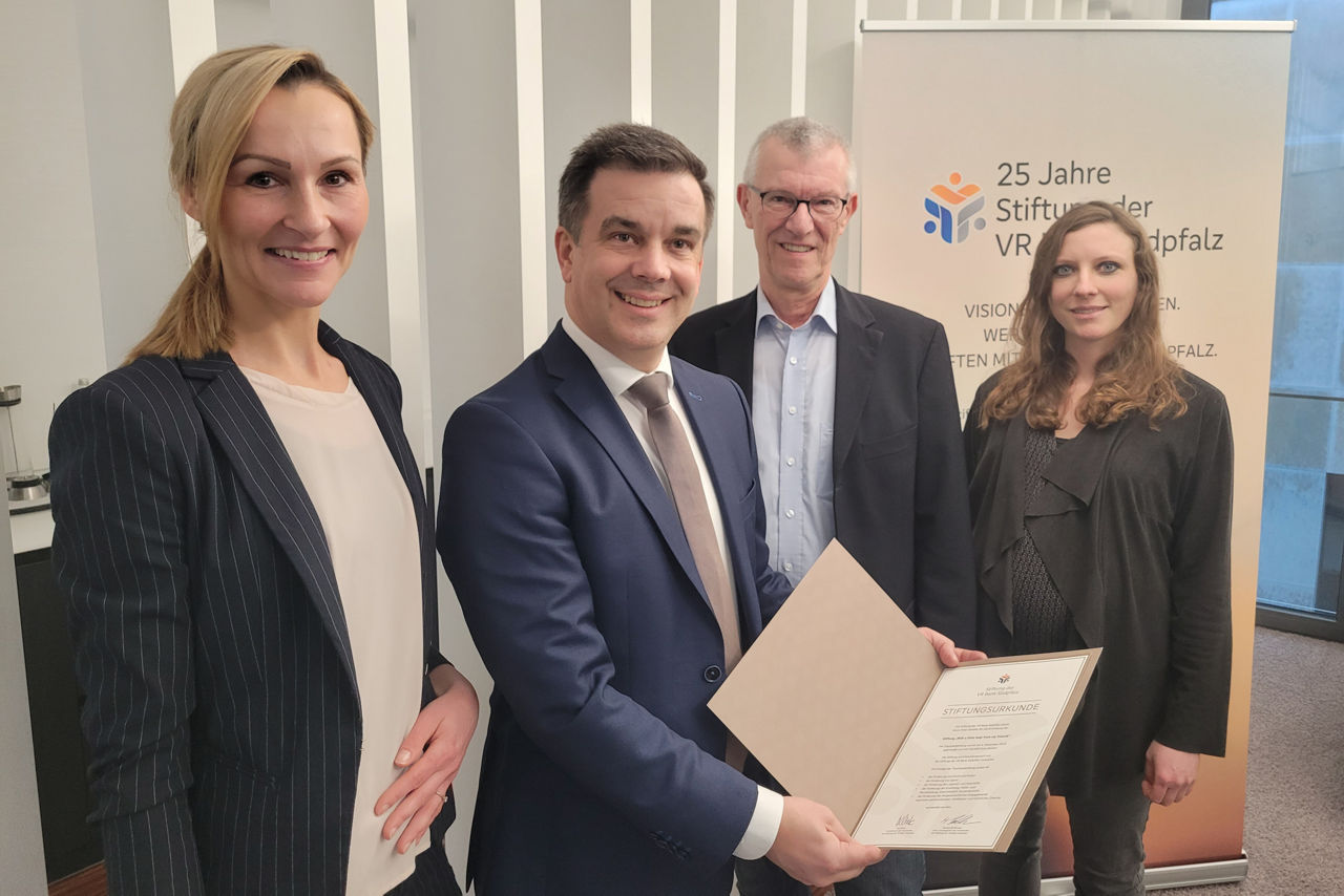 Zwei Frauen und zwei Männer stehen vor einem Banner. Ein Mann hält die Stiftungsurkunde in der Hand.