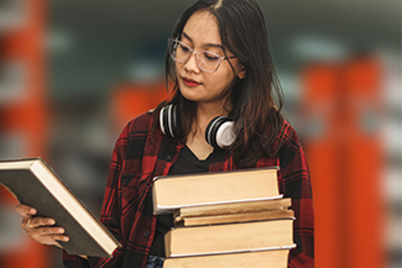 Eine Frau ist in der Bücherei und hält einen Stapel Bücher in den Händen.