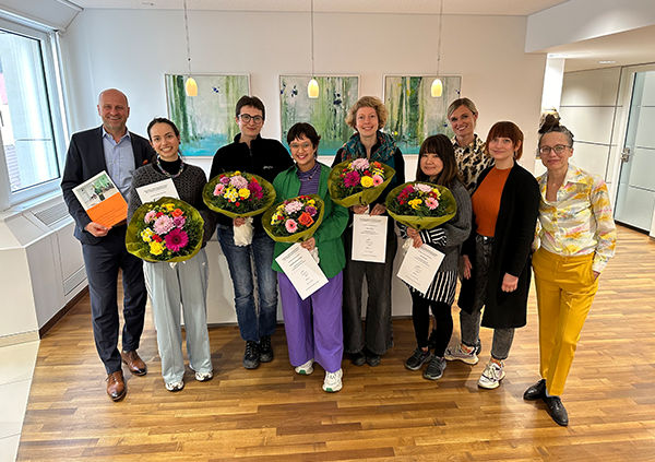 In einer Reihe stehen neun Frauen und ein Mann, die Frauen halten Blumensträuße in der Hand, weil sie geehrt wurden
