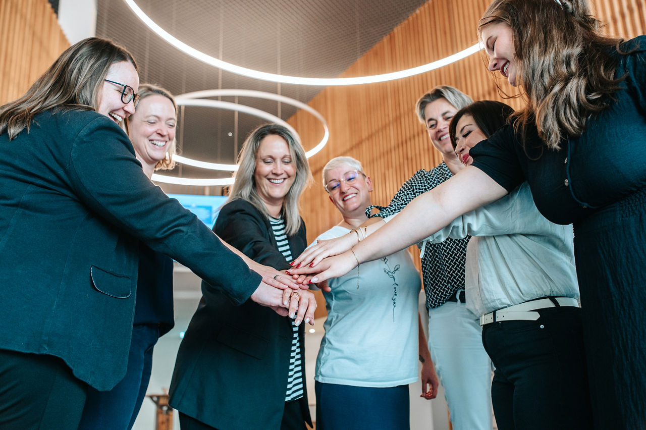 Eine fröhliche Gruppe von Frauen, die ihre Hände im Kreis zusammenlegen.