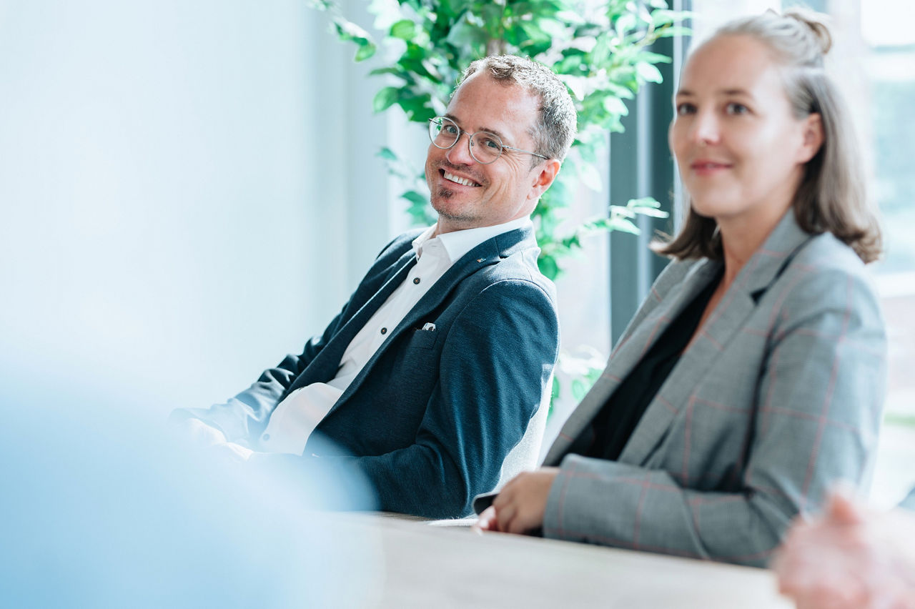Zwei lächelnde Personen sitzen nebeneinander in einem Büro