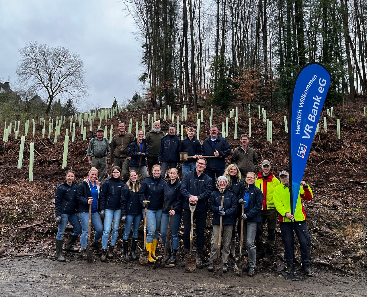 Mitgliederwald Leichlingen - Foto: 19 Personen stehen teils mit Schaufeln vor einem Waldhang mit neu gepflanzten Bäumen