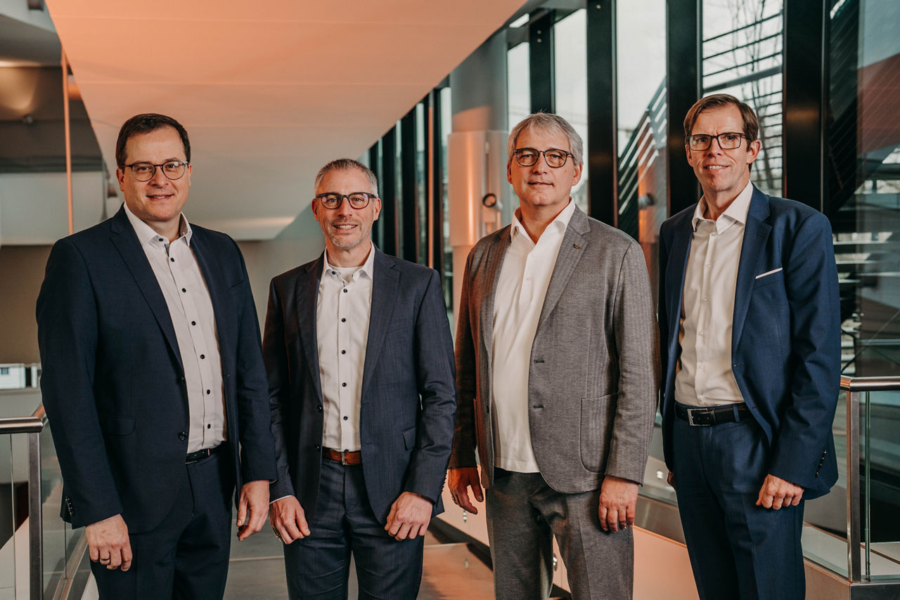 Vier Personen stehen in einem Bankgebäude zu einem Gruppenbild zusammen.