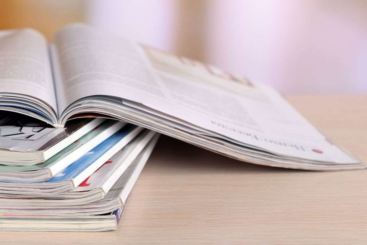 Zeitschriften gestappelt auf einem Holztisch.