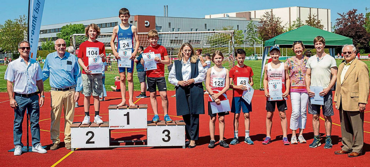 Siegerehrung im Wettbewerb Hochsprung. Drei junge Männer stehen auf dem Podium mit Urkunde. Ehrengäste umgeben sie.