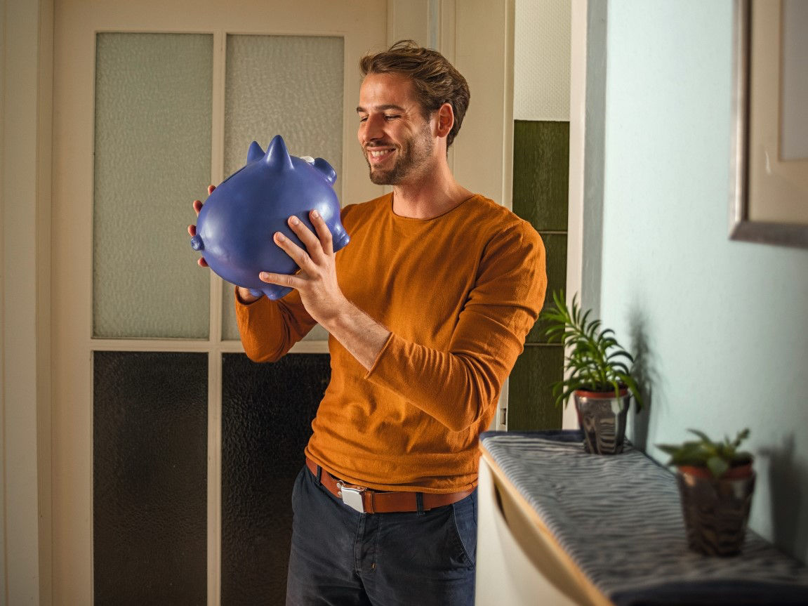 Ein Mann hält ein Sparschwein in der Hand.