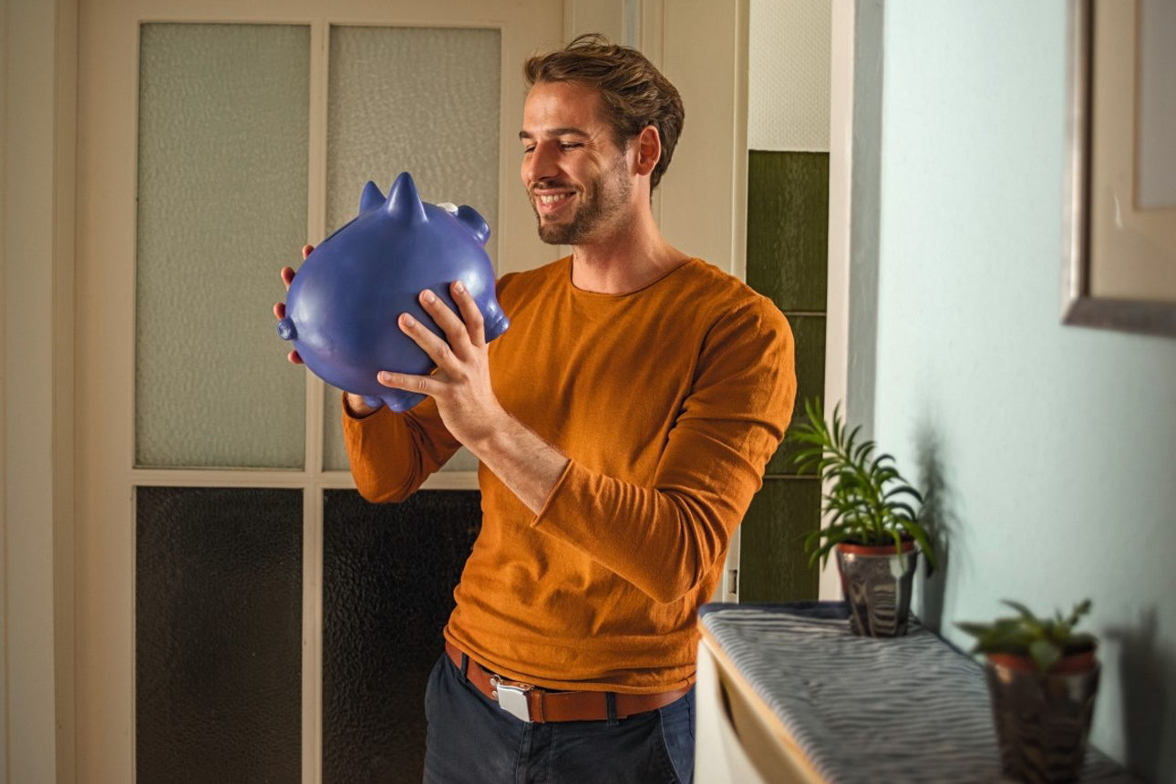 Ein Mann hält ein Sparschwein in der Hand.
