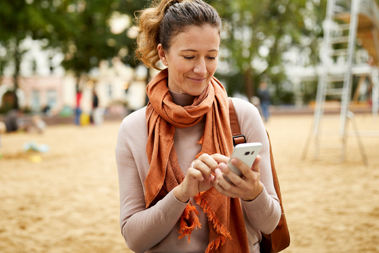 Frau steht mit Handy auf Spielplatz