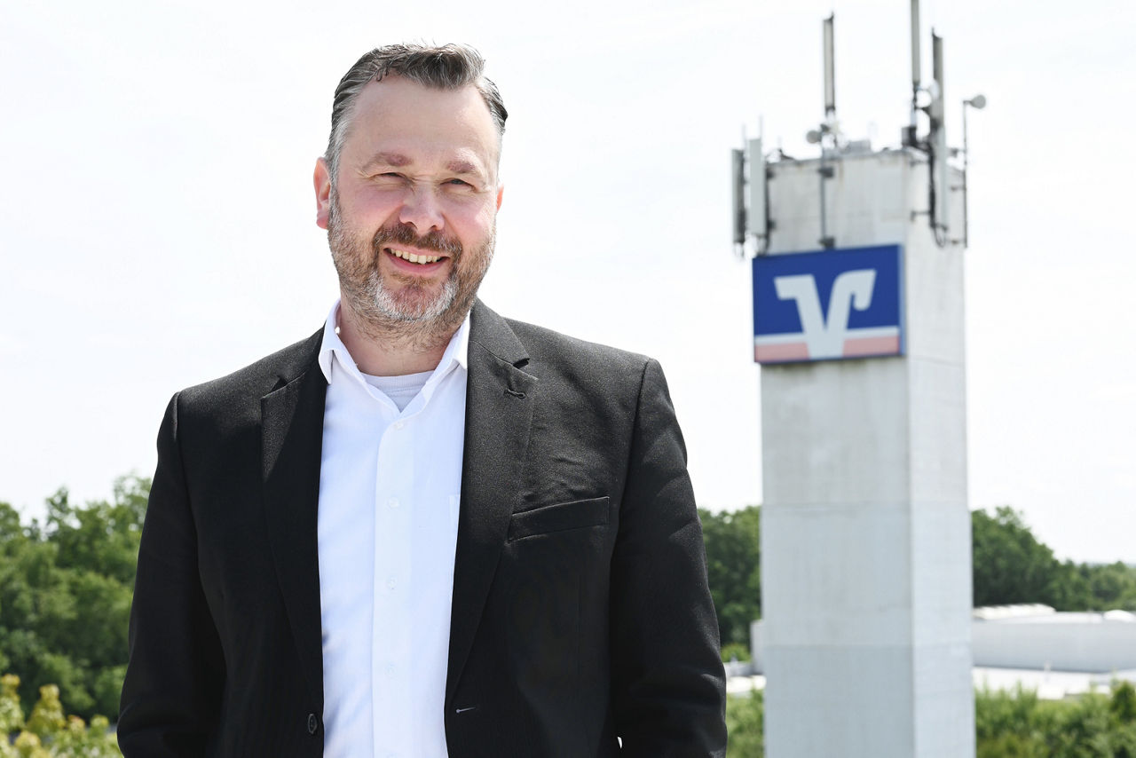 Kollege steht auf Dach vor Volksbank-Logo und Photovoltaikanlage
