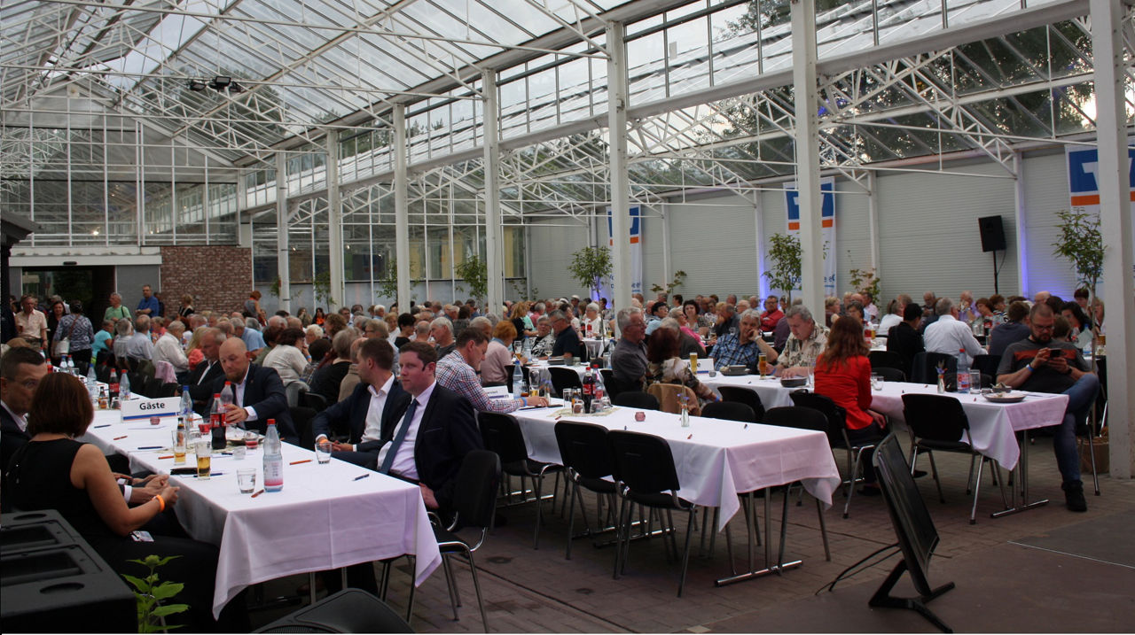 Glashaus mit vielen Menschen am Tisch sitzend