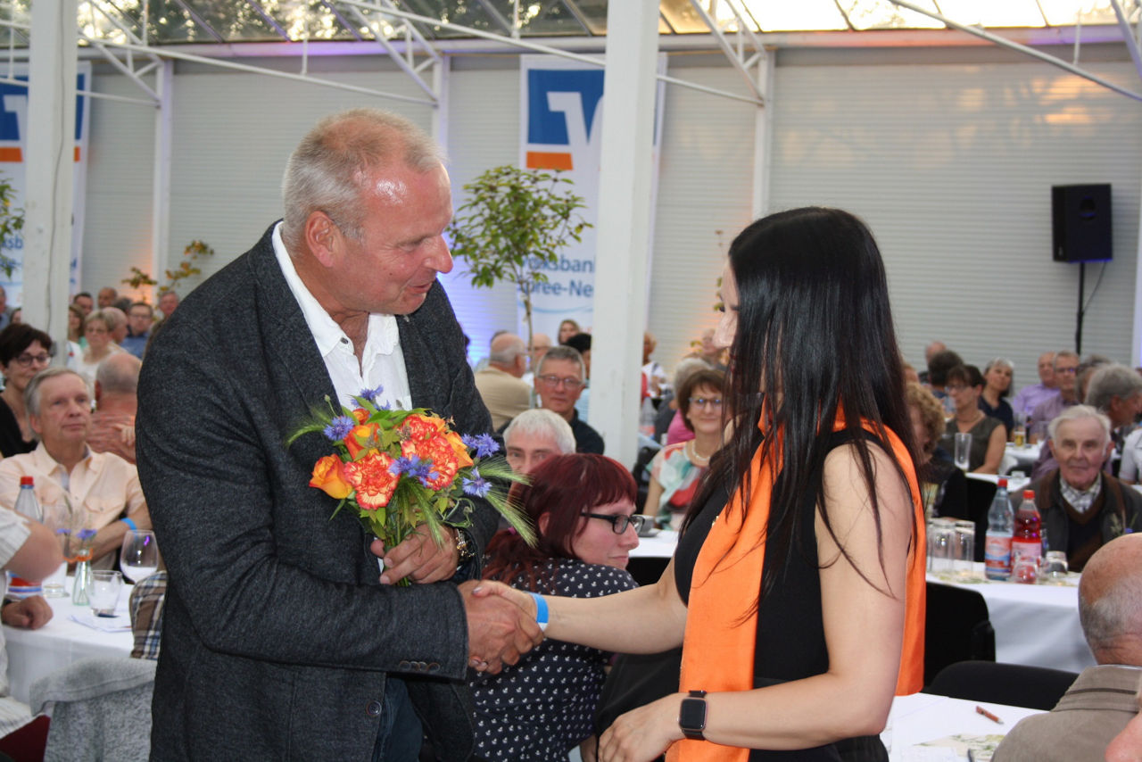 junge Frau gratuliert einem Herren und übergibt einen Blumenstrauß