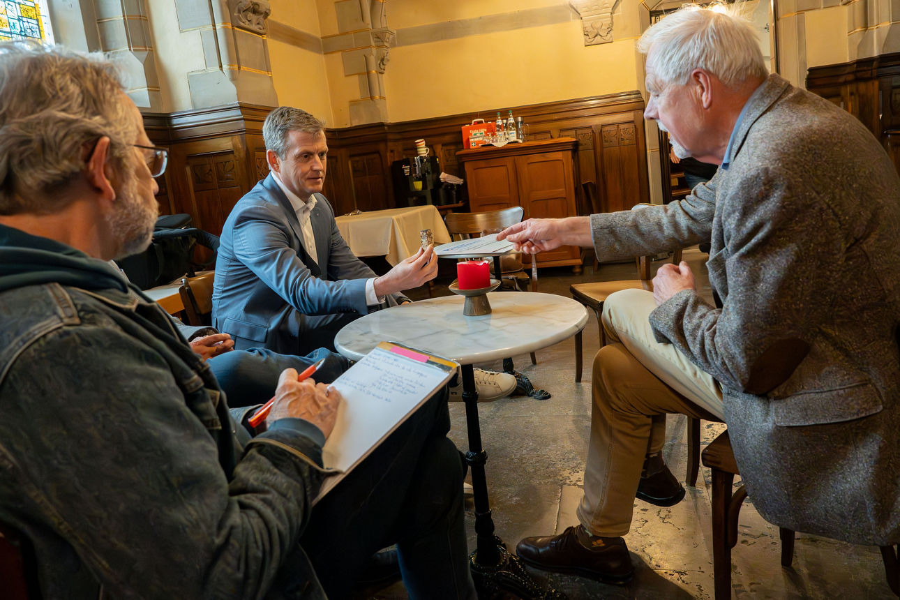 Vier Männer sitzen in einer Kirche. Einer erklärt mit einem Bauteil die Restaurierungspläne.