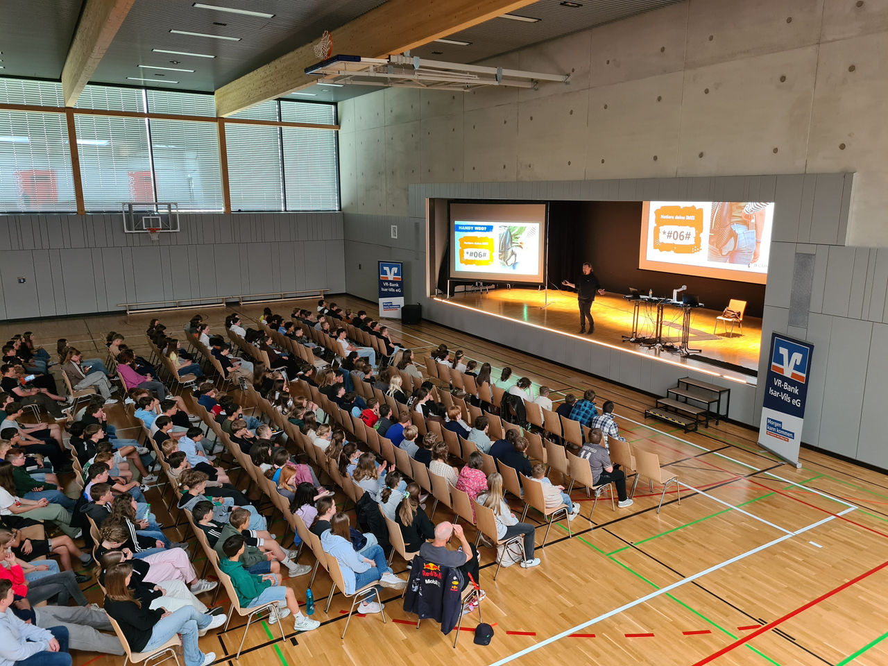 Eine Turnhalle voll mit Schülern, die dem Referenten gespannt zuhören