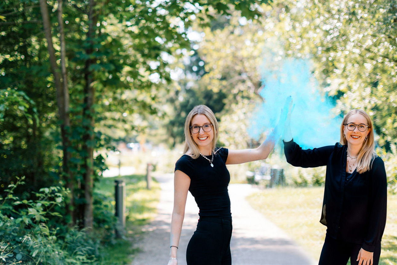 Zwei Frauen klatschen in die Hände und blauer Staub schwebt um sie herum.