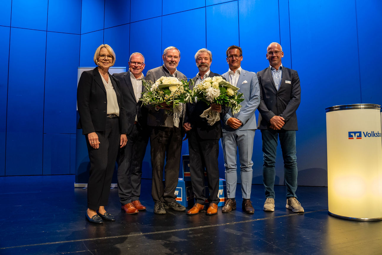 Auf dem Bild ist eine Gruppe von Menschen zu sehen, die zwei Blumensträuße in der Hand halten