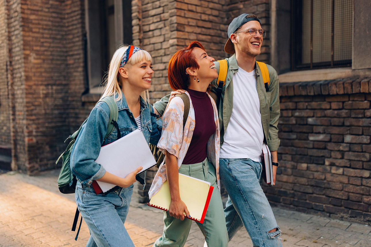Drei junge Menschen gehen mit Schulsachen über Gehweg