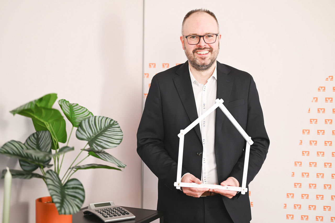 Leiter Baufinanzierung Andreas Stephan mit Zollstock-Haus