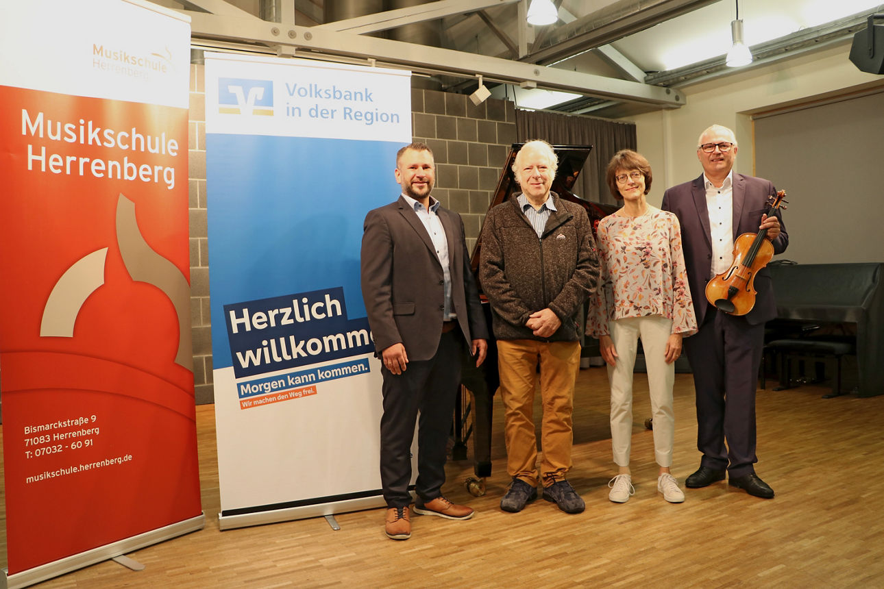 Co-Vorstandssprecher Jörg Stahl steht mit 3 Personen und Geige vor Display der Volksbank und der Musikschule