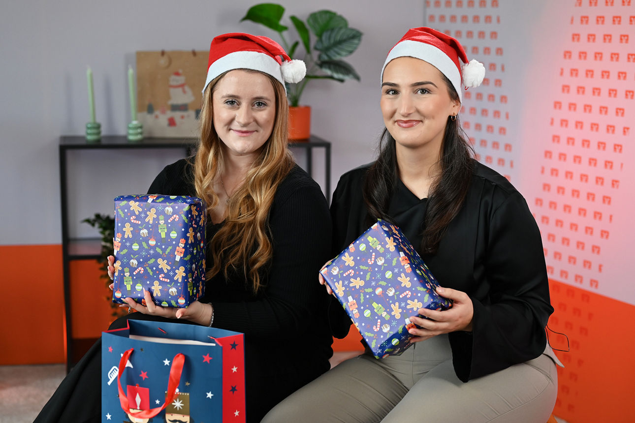 Linda Bingel und Ulvije Osmani sitzen mit Weihnachtsmützen und Geschenken im Videostudio