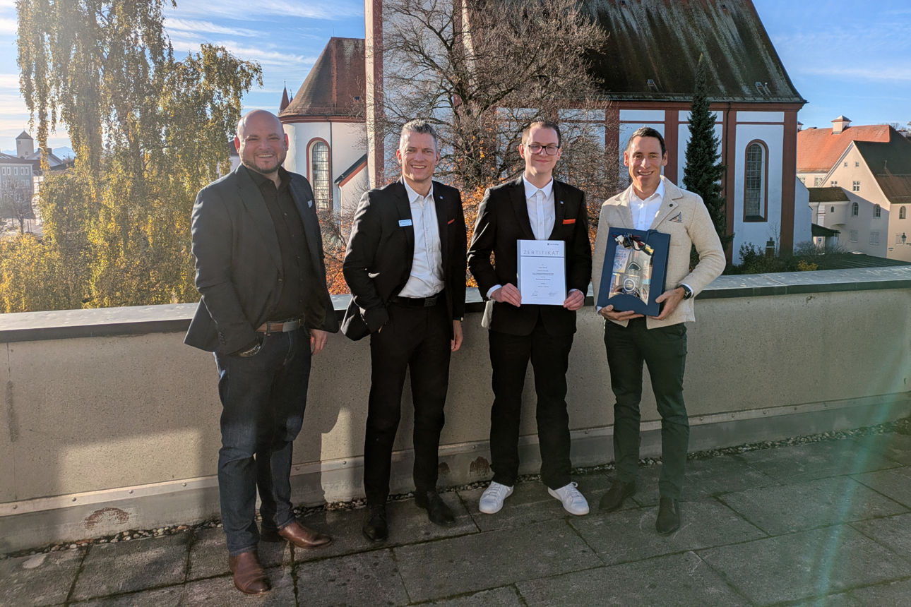 Mitarbeiter mit Urkunde in der Hand steht zusammen mit Führungskräften auf einer Dachterrasse