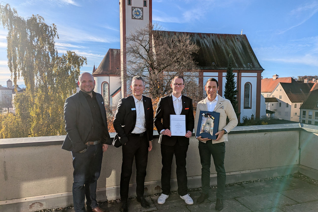 Mitarbeiter mit Urkunde in der Hand steht zusammen mit Führungskräften auf einer Dachterrasse