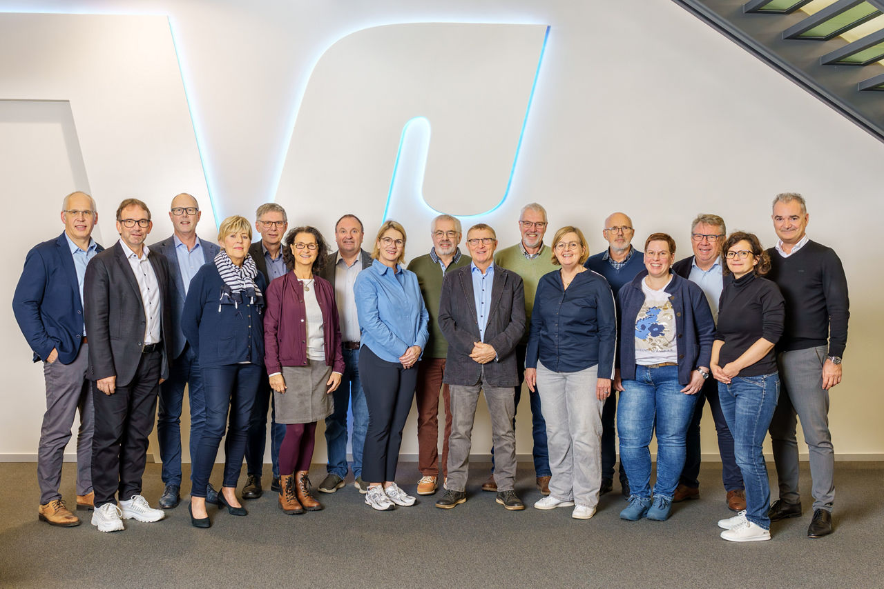 Gruppe von 15 Personen steht vor einer großen, beleuchteten Wand mit VR-Logo