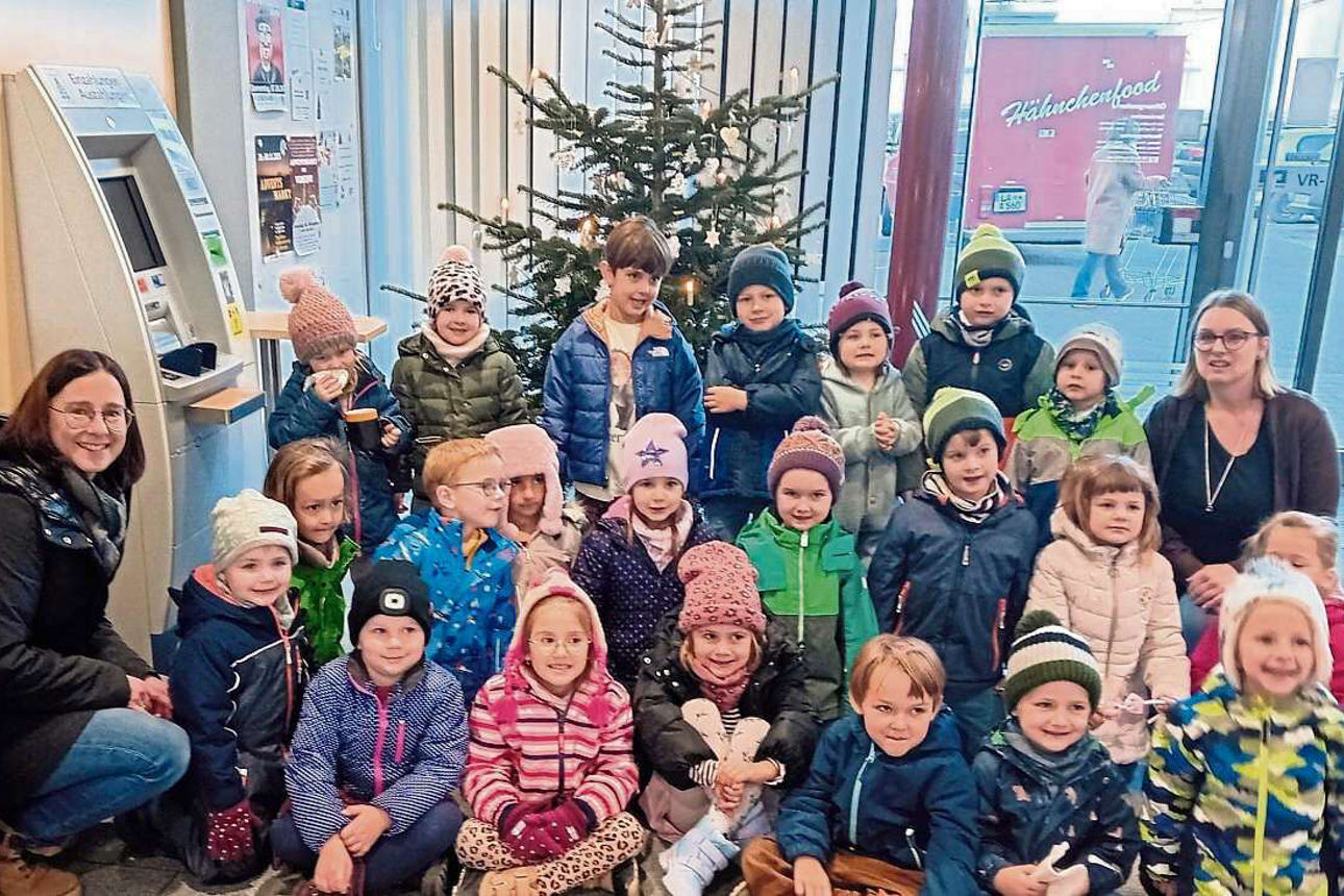 Eine Gruppe von Kindergartenkinder sitzen vor einem geschmückten Christbaum mit ihren Betreuerinnen