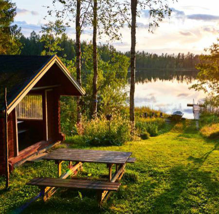 Das Bild zeigt eine Hütte am See.  Es sind auch Bäume und ein See zu sehen. Das Bild sieht idyllisch aus.