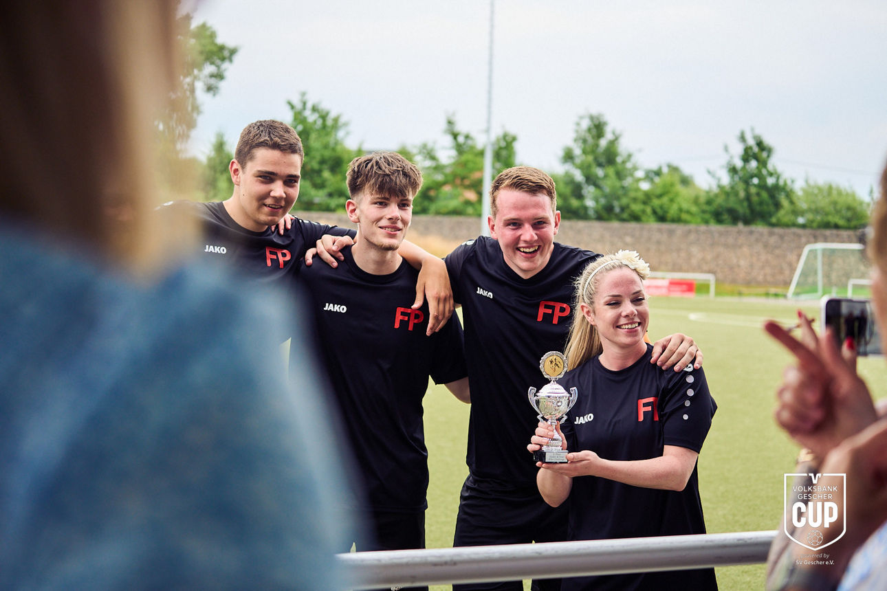 Mehrere Personen stehen nebeneinander und präsentieren einen Pokal