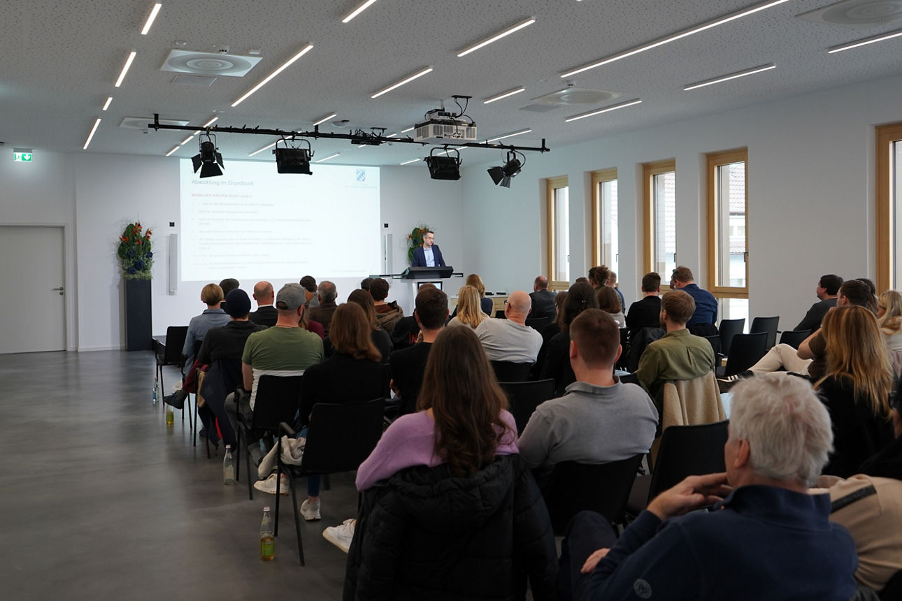 Menschen sitzen auf Stühlen und verfolgen einen Vortrag