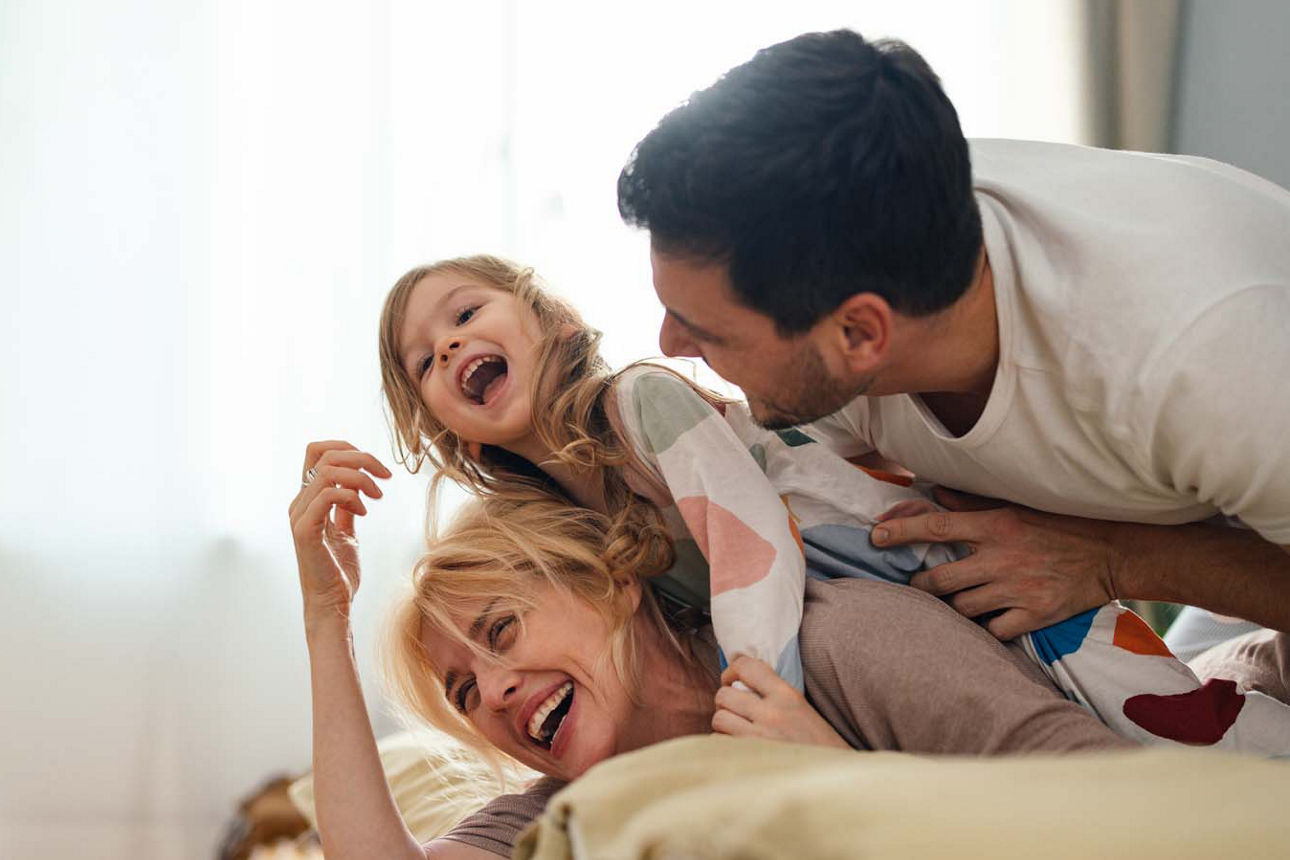 Ein junges Paar spielt mit ihrer Tochter lachend auf dem Bett