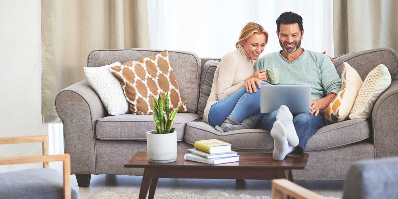 Mann und Frau sitzen glücklich zusammen auf dem Sofa und gucken auf ihren Laptop