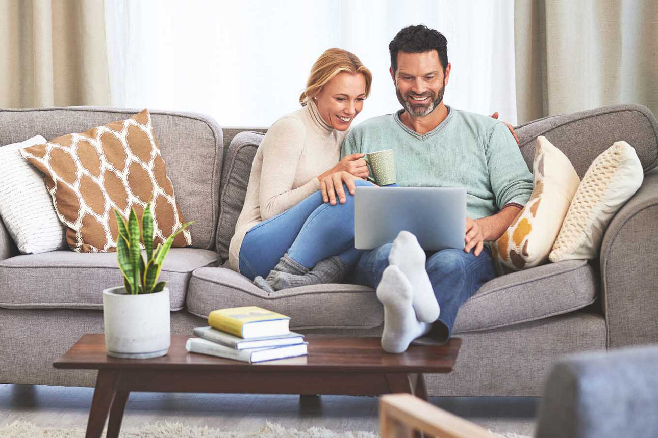 Mann und Frau sitzen glücklich zusammen auf dem Sofa und gucken auf ihren Laptop