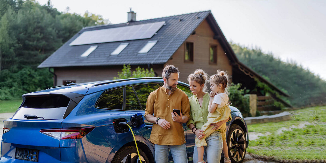 Junge Familie steht vor ihrem Einfamilienhaus mit Solaranlage und Elektroauto