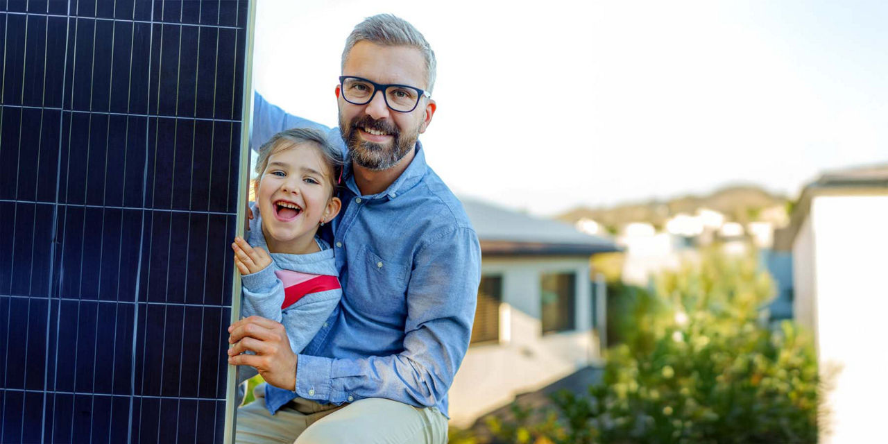 Vater und Tocher lachen gemeinsam. Neben ihnen steht ein Solarmodul