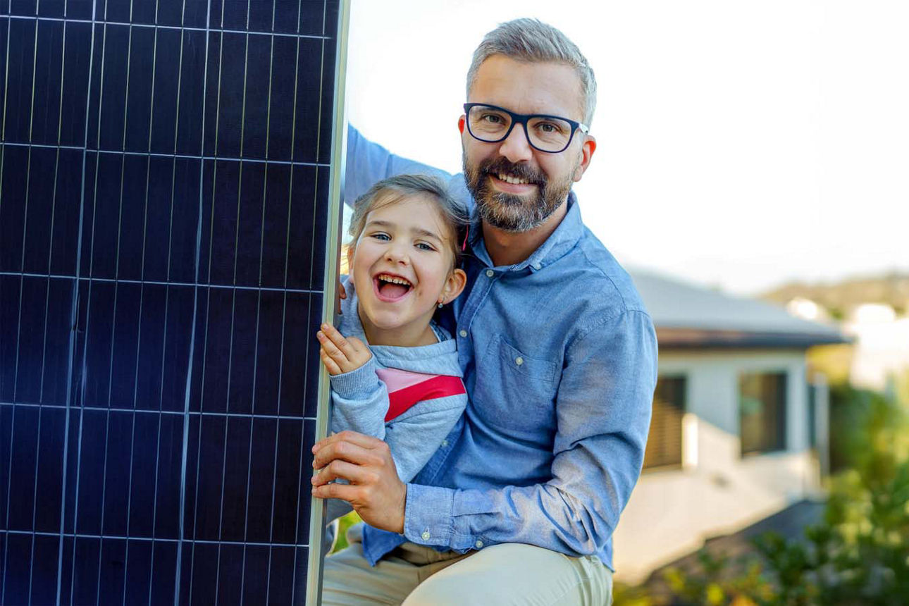 Vater und Tocher lachen gemeinsam. Neben ihnen steht ein Solarmodul