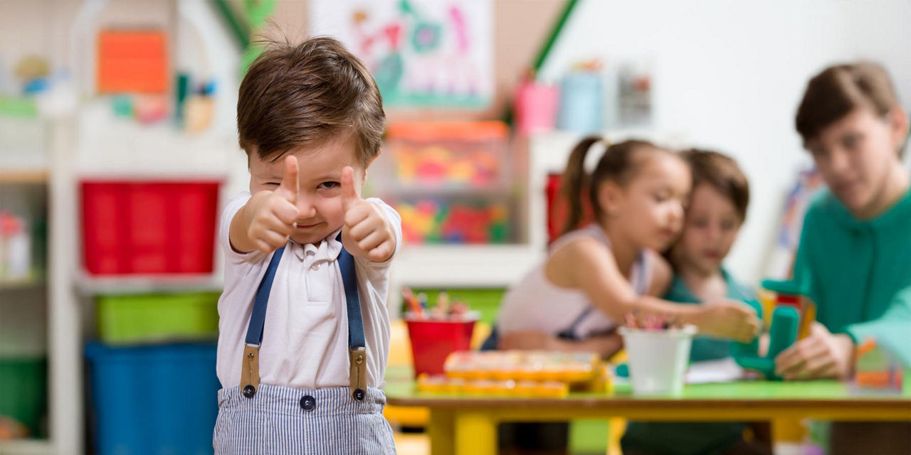 Kleiner Junge zeigt Daumen hoch in die Kamera mit weiteren Kindern im Hintergrund