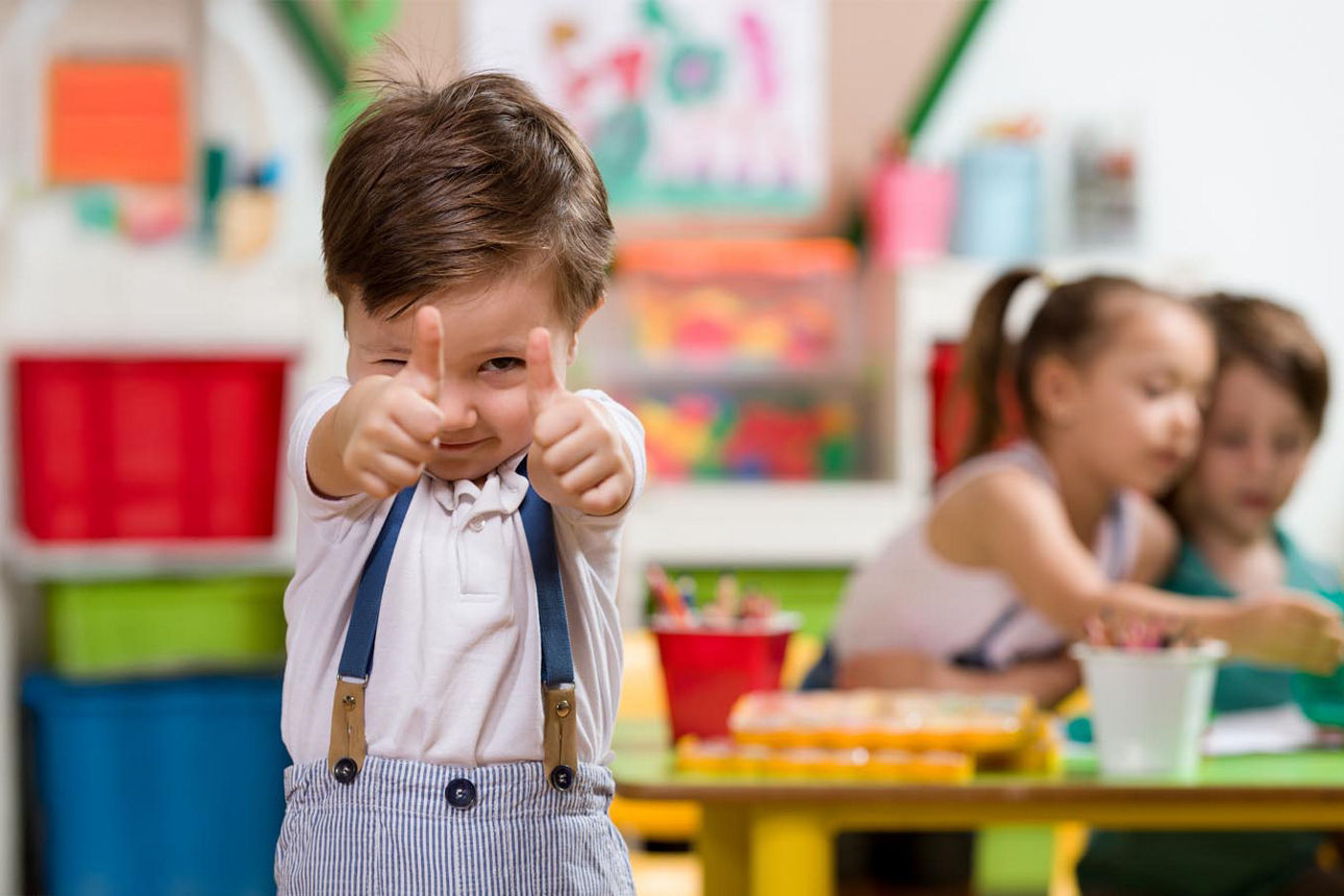 Kleiner Junge zeigt Daumen hoch in die Kamera mit weiteren Kindern im Hintergrund