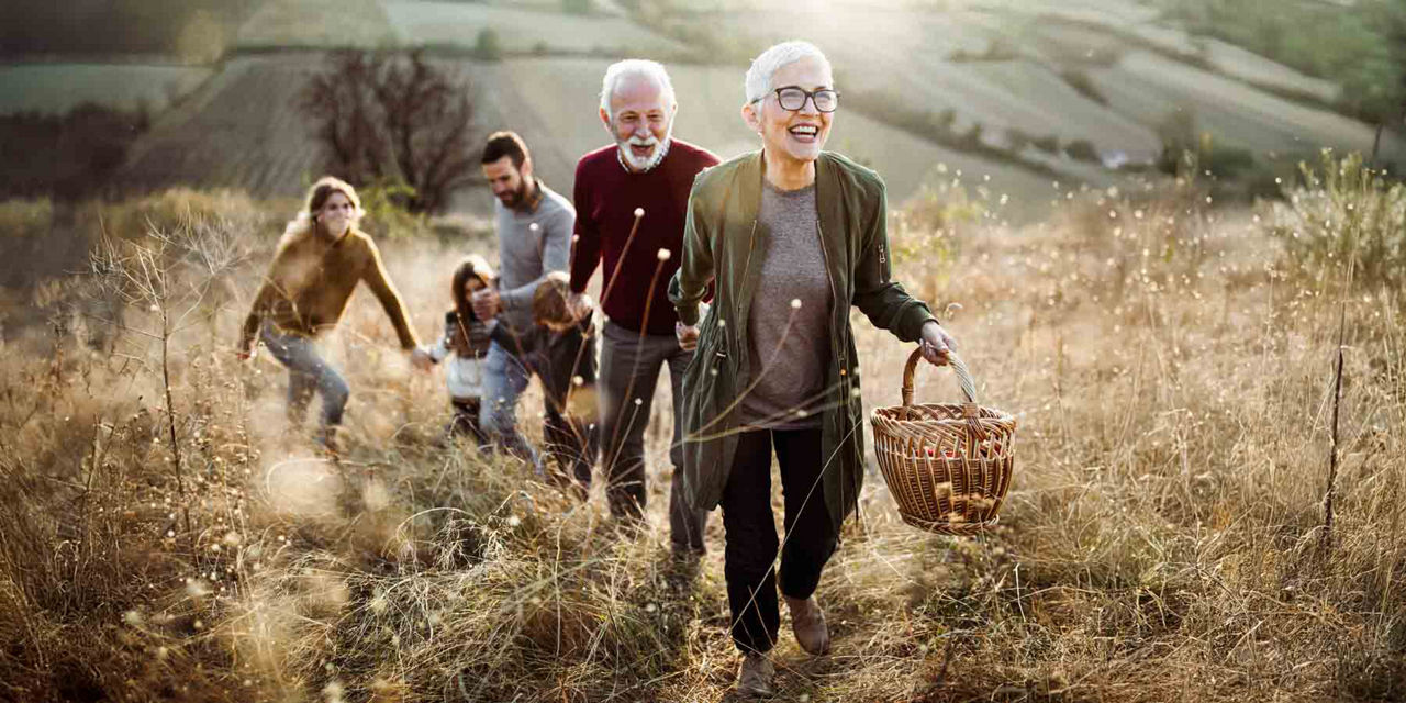 Eine Familie aus Großeltern, Eltern und Kind laufen glücklich über eine Wiese