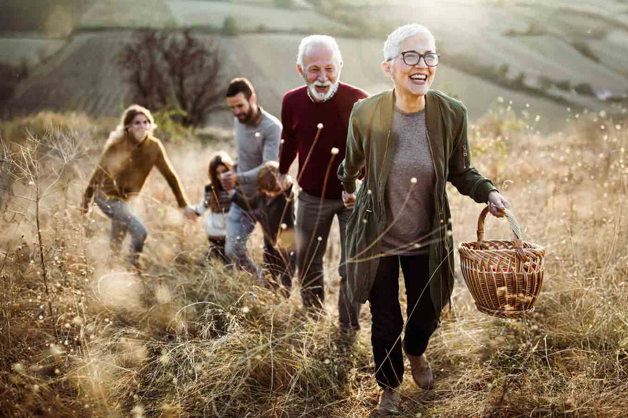 Eine Familie aus Großeltern, Eltern und Kind laufen glücklich über eine Wiese