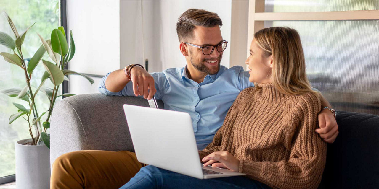 Junger Mann und junge Frau sitzen zusammen auf dem Sofa vor ihrem Laptop