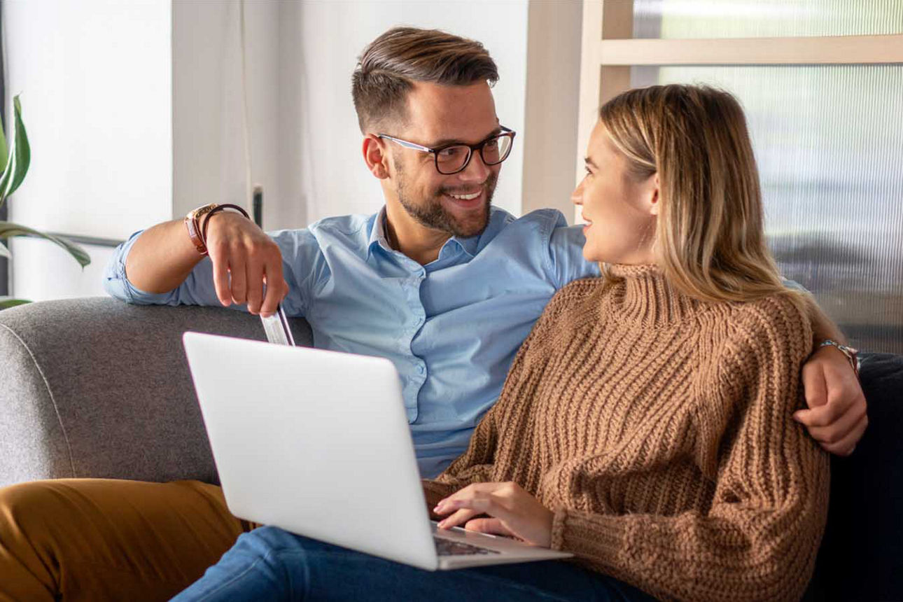 Junger Mann und junge Frau sitzen zusammen auf dem Sofa vor ihrem Laptop
