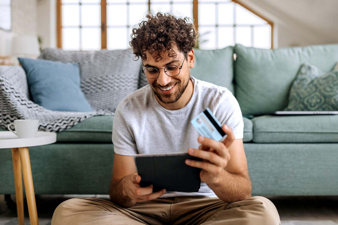 Junger Mann mit Kreditkarte in der Hand schaut zufrieden auf sein Tablet
